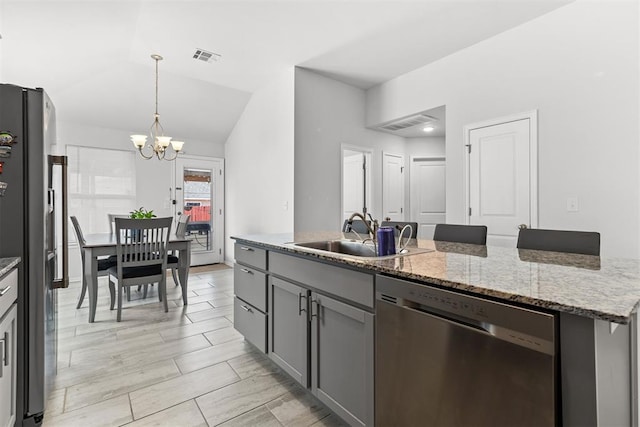 kitchen with lofted ceiling, a sink, hanging light fixtures, appliances with stainless steel finishes, and an island with sink