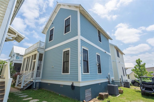 view of side of property featuring a lawn, a sunroom, a balcony, and central AC