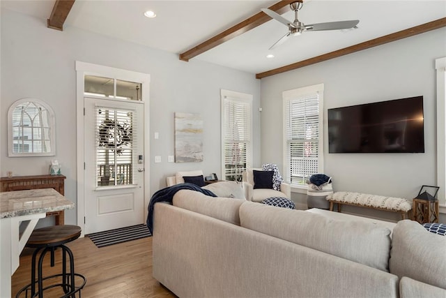 living room with beamed ceiling, light wood-type flooring, a wealth of natural light, and ceiling fan