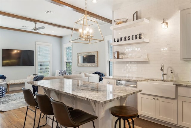 kitchen featuring sink, beamed ceiling, hardwood / wood-style floors, a kitchen bar, and decorative backsplash