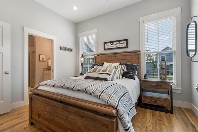 bedroom featuring connected bathroom, multiple windows, and light wood-type flooring