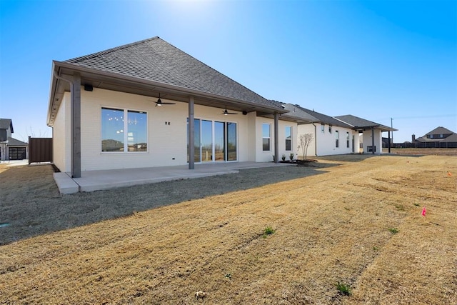 back of property with a ceiling fan, a patio area, a lawn, and a shingled roof