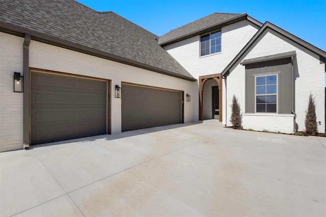 traditional home with a garage, brick siding, and roof with shingles