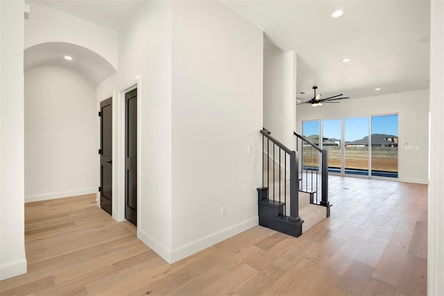 corridor with light wood-style flooring, recessed lighting, baseboards, and arched walkways