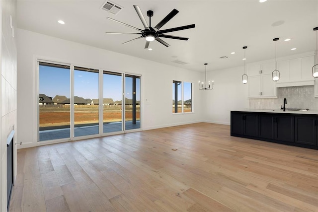 unfurnished living room with visible vents, baseboards, recessed lighting, light wood-style flooring, and ceiling fan with notable chandelier