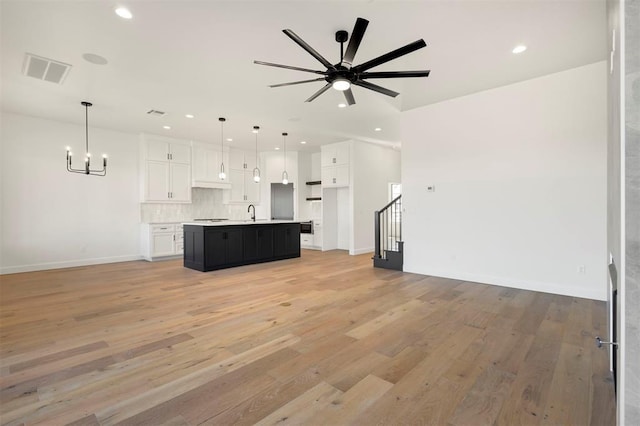 unfurnished living room with light wood finished floors, visible vents, stairs, ceiling fan with notable chandelier, and recessed lighting