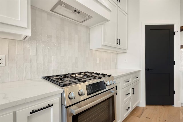 kitchen featuring tasteful backsplash, white cabinetry, stainless steel gas range, and wall chimney exhaust hood