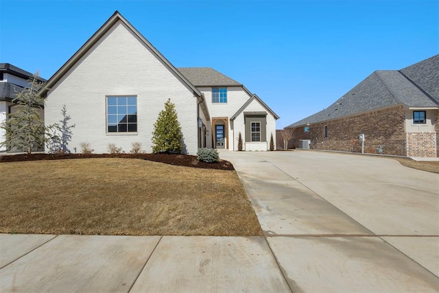 view of front of home featuring a front lawn, central AC unit, brick siding, and roof with shingles