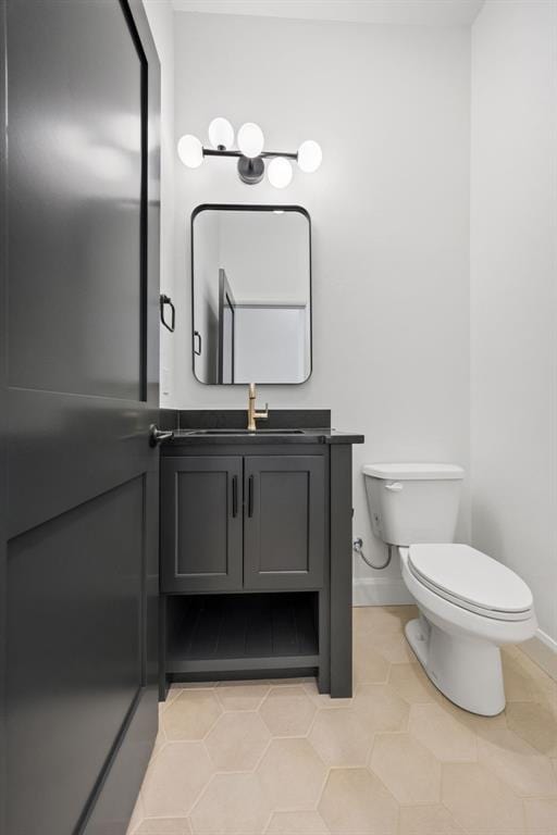 half bath with tile patterned flooring, toilet, vanity, and baseboards