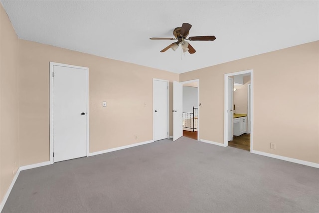 unfurnished bedroom with a closet, ensuite bathroom, dark carpet, and ceiling fan