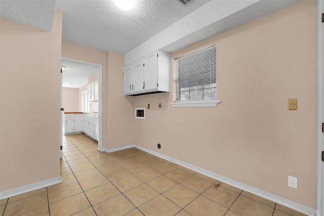 clothes washing area featuring electric dryer hookup, cabinets, washer hookup, light tile patterned floors, and a textured ceiling