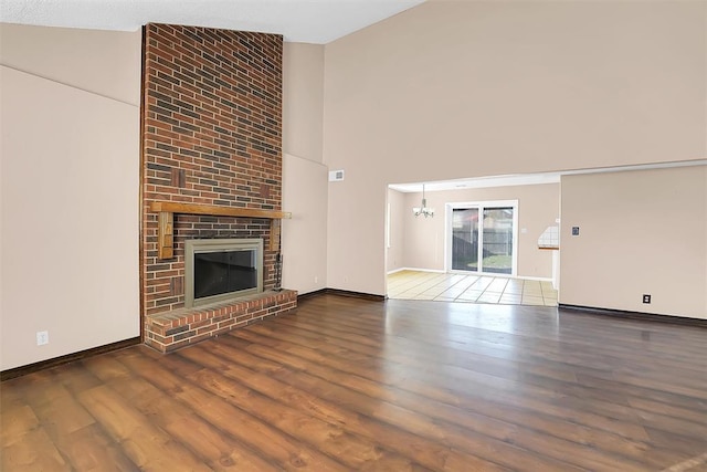 unfurnished living room with a fireplace, dark hardwood / wood-style flooring, high vaulted ceiling, and a chandelier