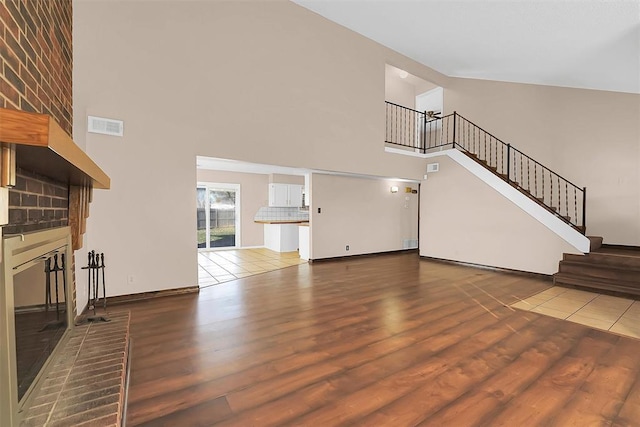 unfurnished living room featuring a fireplace, high vaulted ceiling, and hardwood / wood-style flooring