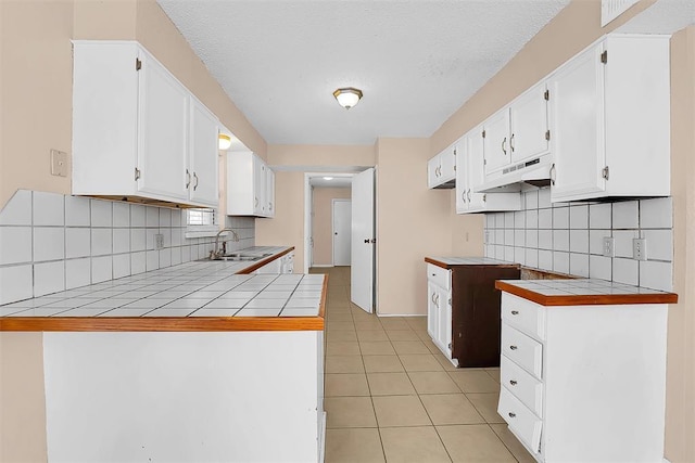 kitchen with white cabinets, sink, decorative backsplash, light tile patterned floors, and tile counters