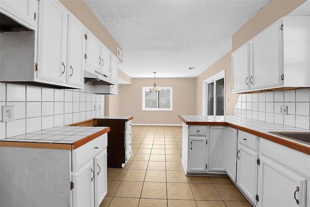 kitchen featuring tile countertops, decorative backsplash, white cabinets, and hanging light fixtures