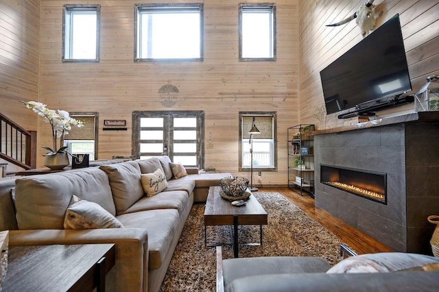 living room with french doors, a tile fireplace, hardwood / wood-style flooring, a high ceiling, and wood walls