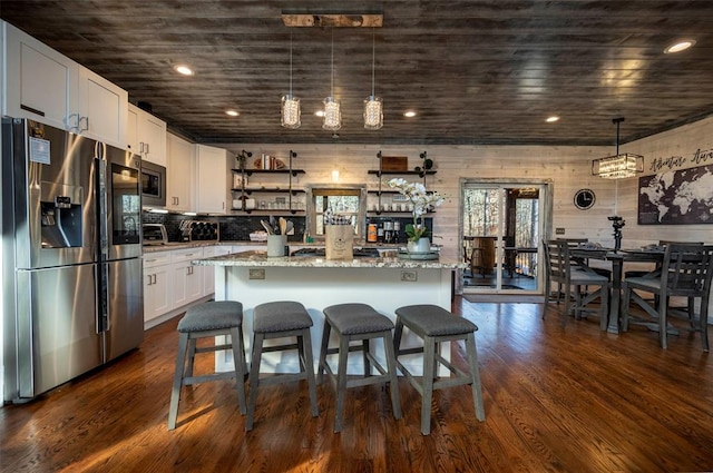 kitchen with a center island, stainless steel appliances, white cabinetry, and light stone counters