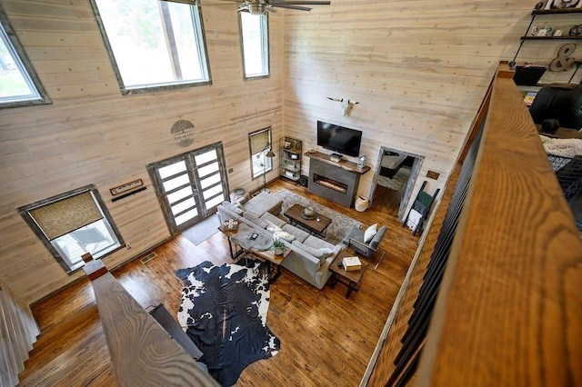 living room with wooden walls, a towering ceiling, ceiling fan, and wood-type flooring