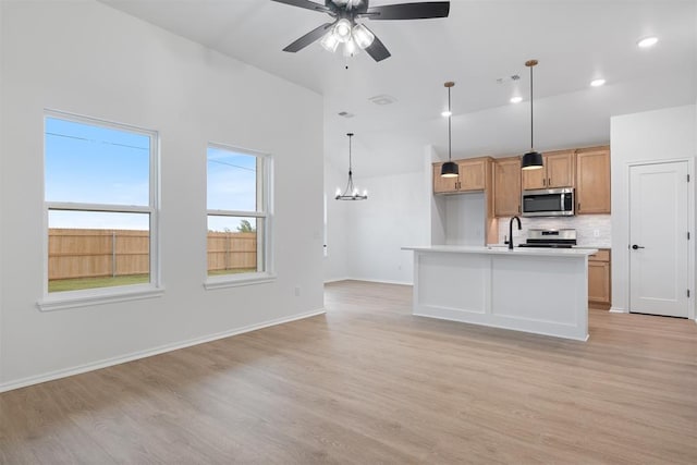 kitchen featuring stainless steel appliances, light hardwood / wood-style floors, decorative light fixtures, a center island with sink, and ceiling fan with notable chandelier