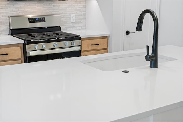 kitchen with light brown cabinets, backsplash, stainless steel range with gas cooktop, and sink