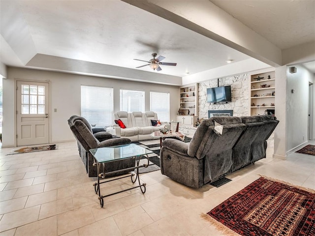 living room with built in shelves, ceiling fan, a stone fireplace, and light tile patterned floors