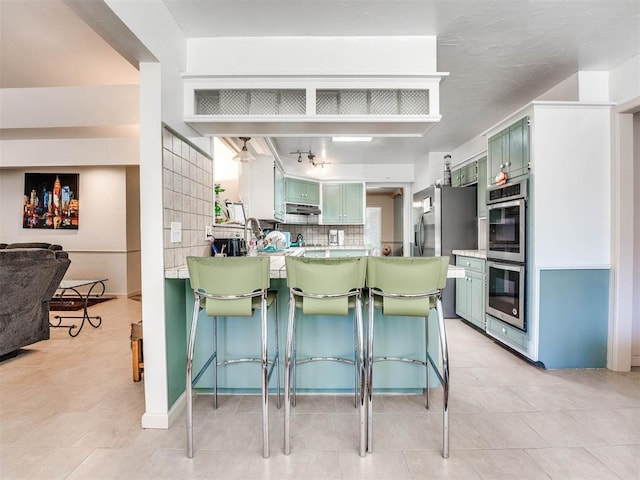 kitchen featuring a breakfast bar, kitchen peninsula, green cabinetry, and tasteful backsplash