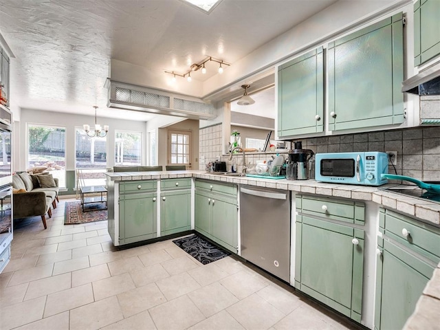 kitchen with dishwasher, green cabinets, hanging light fixtures, tasteful backsplash, and tile counters