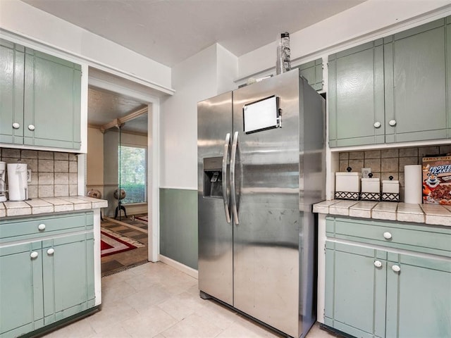 kitchen featuring decorative backsplash, stainless steel refrigerator with ice dispenser, tile countertops, green cabinets, and light tile patterned flooring