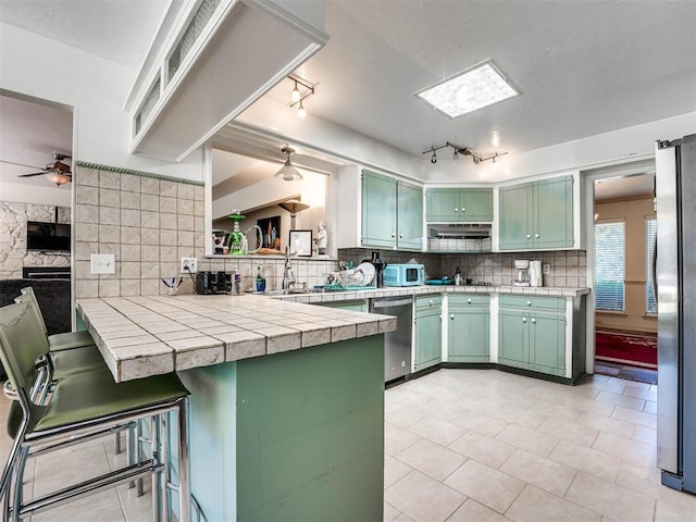 kitchen featuring green cabinetry, appliances with stainless steel finishes, tasteful backsplash, kitchen peninsula, and a breakfast bar area