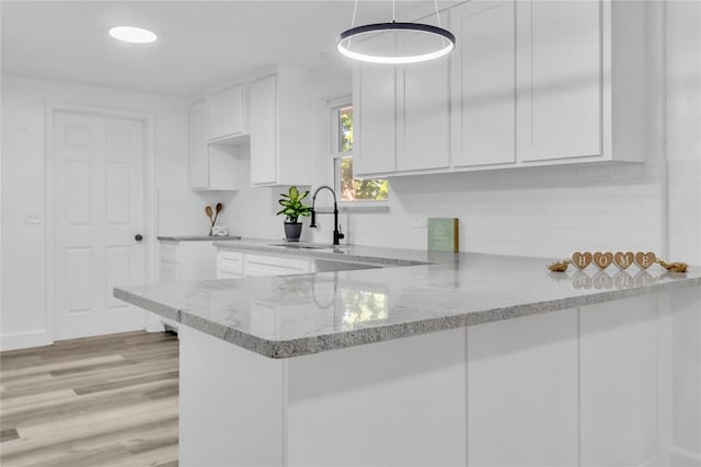 kitchen with light stone counters, kitchen peninsula, sink, and white cabinets