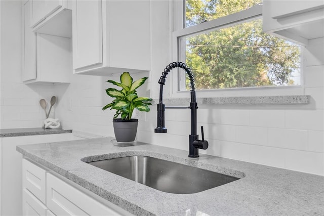 room details with white cabinetry, light stone counters, sink, and tasteful backsplash