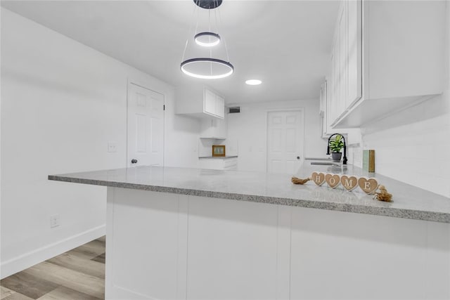 kitchen with sink, white cabinetry, light hardwood / wood-style floors, decorative light fixtures, and kitchen peninsula