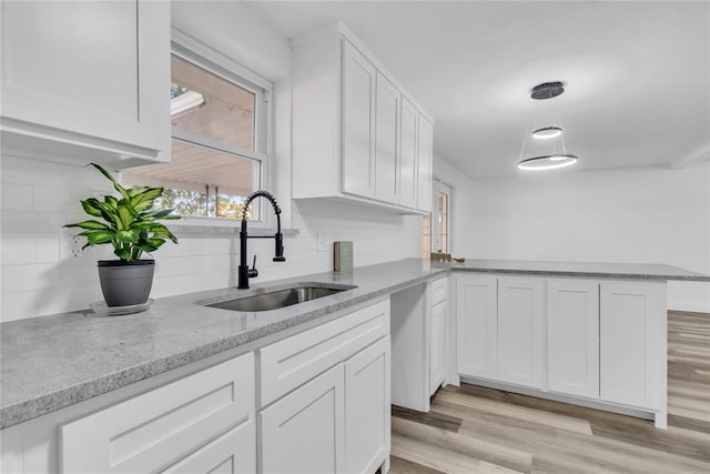 kitchen with sink, white cabinetry, pendant lighting, light hardwood / wood-style floors, and decorative backsplash