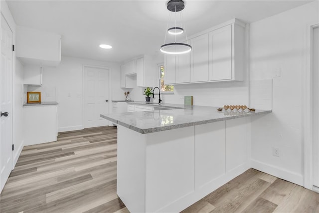 kitchen with decorative light fixtures, sink, white cabinets, kitchen peninsula, and light wood-type flooring