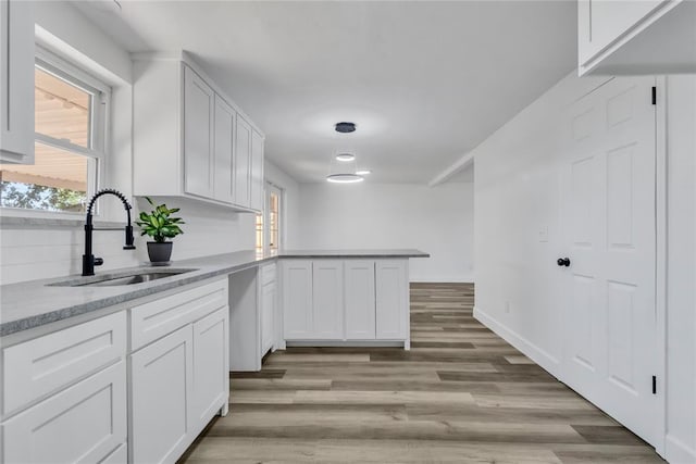 kitchen with sink, light hardwood / wood-style flooring, kitchen peninsula, and white cabinets