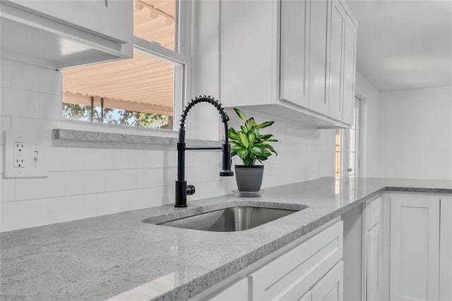 kitchen with light stone countertops, sink, white cabinets, and decorative backsplash