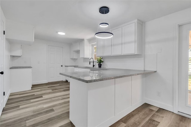 kitchen with decorative light fixtures, sink, white cabinets, kitchen peninsula, and light wood-type flooring