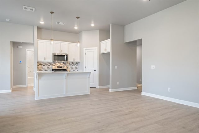 kitchen with hanging light fixtures, light hardwood / wood-style flooring, a center island with sink, white cabinets, and appliances with stainless steel finishes