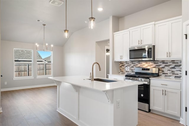 kitchen featuring a kitchen island with sink, white cabinets, stainless steel appliances, and decorative light fixtures