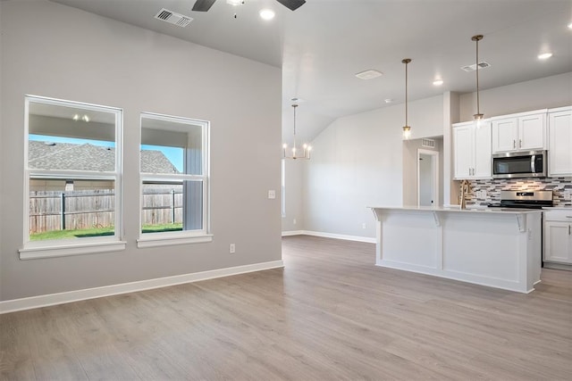 kitchen with hanging light fixtures, stainless steel appliances, white cabinets, ceiling fan with notable chandelier, and light wood-type flooring