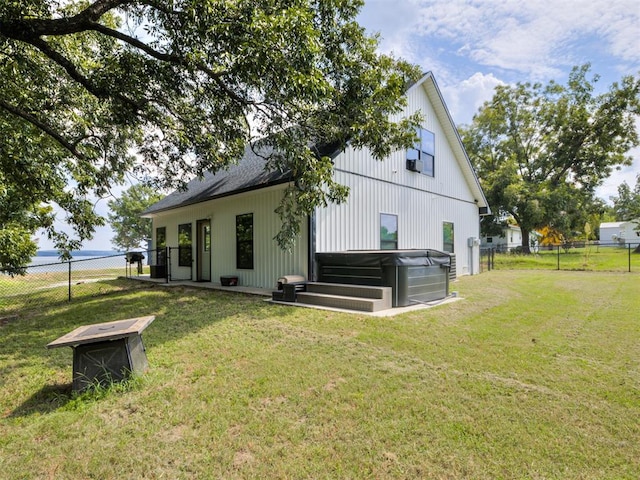 rear view of house featuring a hot tub and a lawn