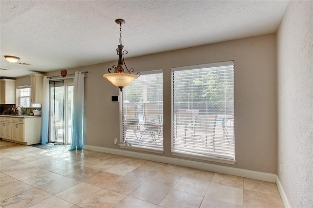 unfurnished dining area with a wealth of natural light, sink, light tile patterned floors, and a textured ceiling