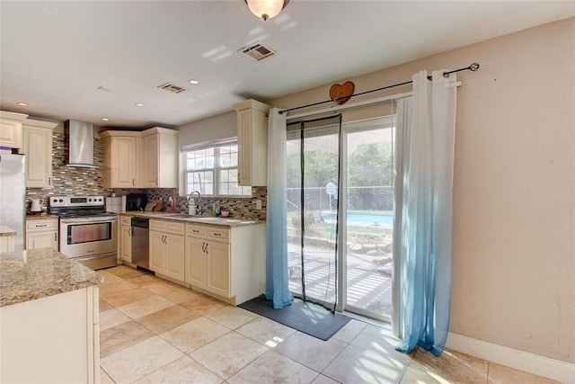 kitchen with light stone countertops, sink, wall chimney range hood, backsplash, and appliances with stainless steel finishes