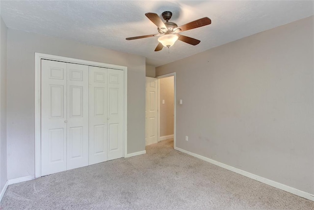 unfurnished bedroom with a textured ceiling, a closet, light colored carpet, and ceiling fan