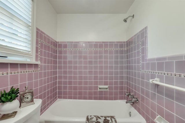 bathroom featuring tiled shower / bath combo, toilet, and tile walls