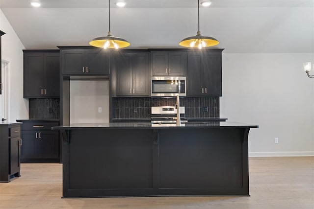 kitchen with appliances with stainless steel finishes, tasteful backsplash, pendant lighting, and an island with sink