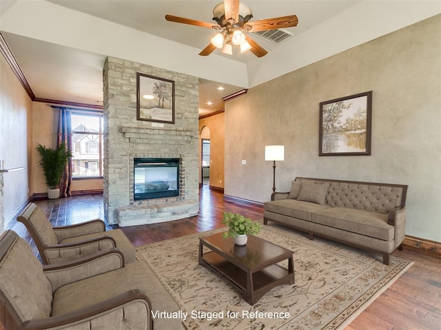 living room featuring hardwood / wood-style flooring, a stone fireplace, ceiling fan, and crown molding