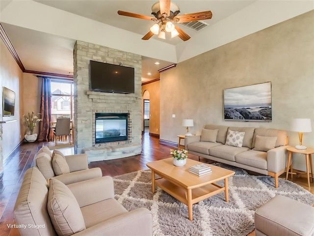 living room with visible vents, ornamental molding, wood finished floors, a stone fireplace, and baseboards