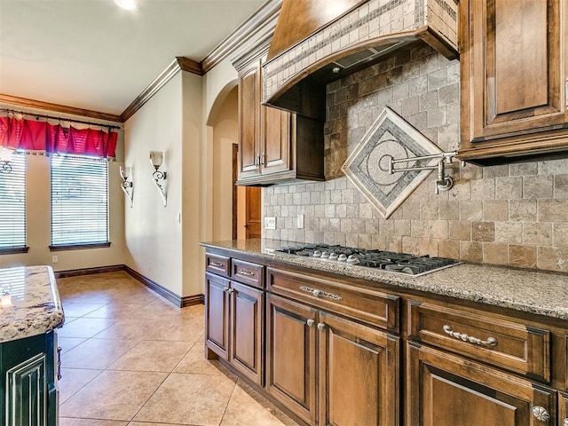 kitchen featuring tasteful backsplash, stainless steel gas stovetop, light tile patterned flooring, crown molding, and baseboards