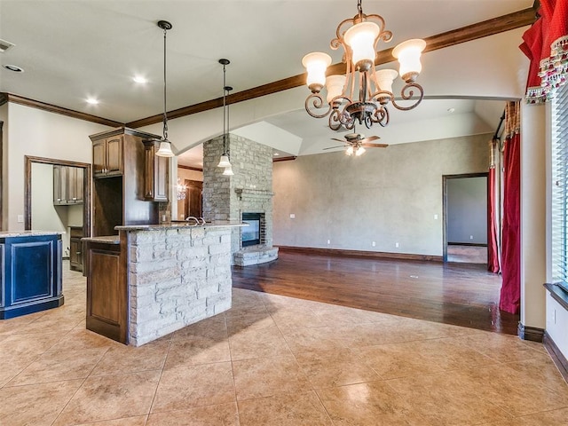 kitchen with a large fireplace, baseboards, open floor plan, ornamental molding, and ceiling fan with notable chandelier